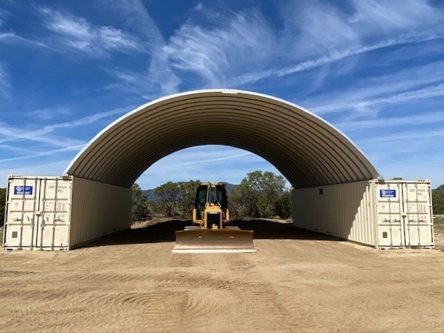 SteelMaster shipping container roof shelter covering a large excavator between two shipping containers